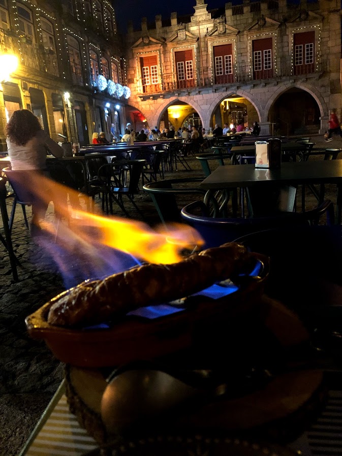 Grilling chouriço over a flame at the table in Guimarães old town