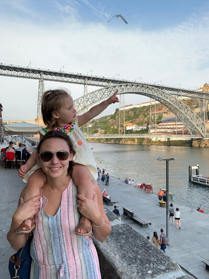 Toddler on Summer's shoulders with the Dom Luís I Bridge behind them in Porto