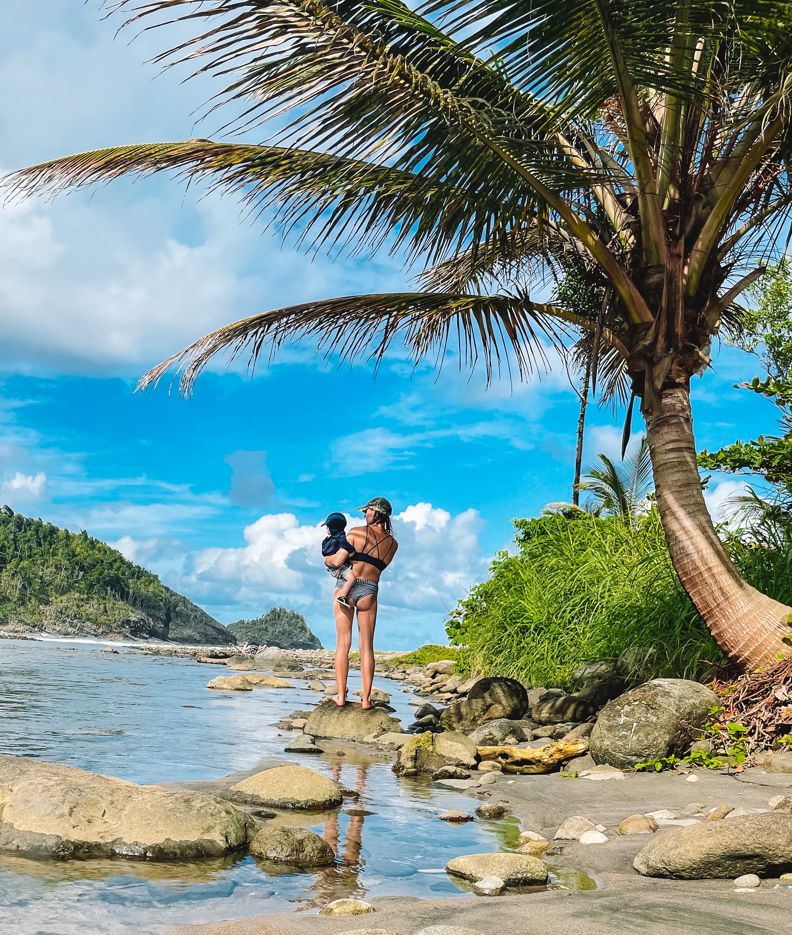 Summer holding her son on the rocks at the water's edge in Dominica