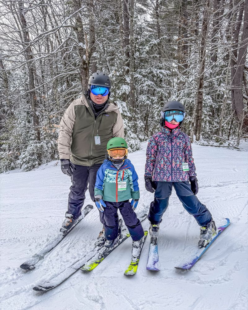 A dad and two kids on skis on a snowy trail at King Pine
