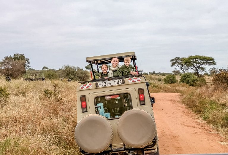 A family looking out of the pop-top roof of a safari Land Cruiser on a red dirt road