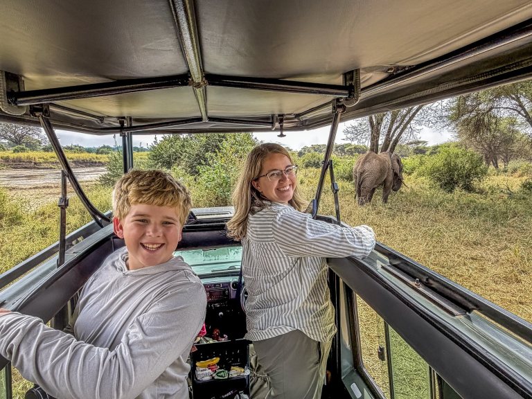 A boy and his mom standing in the pop-top with an elephant behind them in Tarangire
